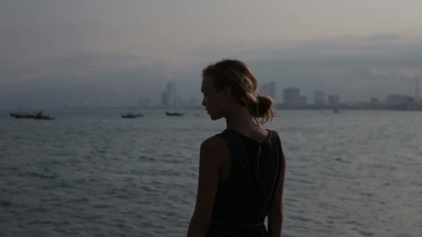 Молодая женщина, стоящая на пляже на камнях и наблюдающая за морем — стоковое видео