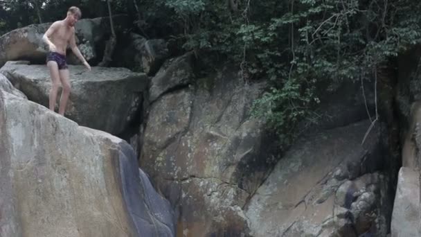 Joven saltando desde las rocas de la cascada en el agua — Vídeos de Stock