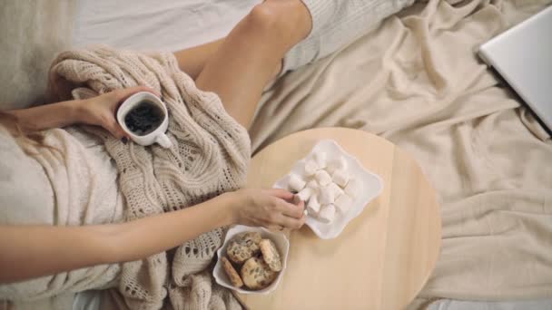 Женщина в теплом свитере на кровати с чашкой кофе в руках, новогодняя елка верхней точки съемки — стоковое видео