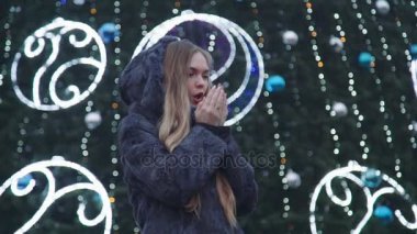 Noel gecesi smiles kamera önünde park ağaçlar bakarak çekici kadın parlak ışıklar dekore edilmiştir.