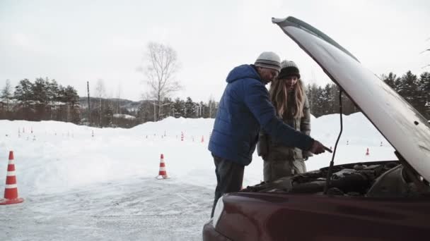 Istruttore di guida Parla del motore di un cofano di un'auto aperta a una ragazza piuttosto adolescente seduta in auto — Video Stock