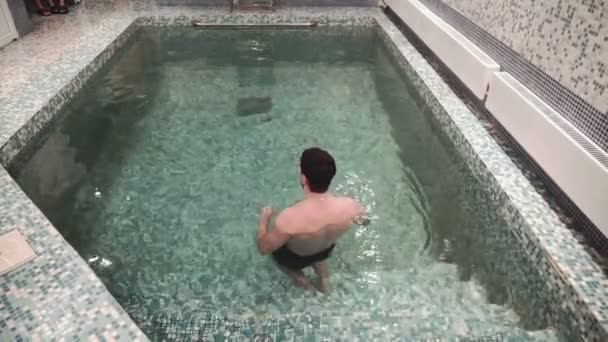 Jovens homens relaxam e saltam, nadam na piscina na sauna — Vídeo de Stock