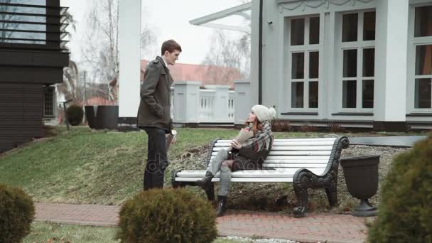 Романтическая молодая пара, сидящая на белой скамейке, в пальто и шляпе, холодная погода, стиль жизни — стоковое видео