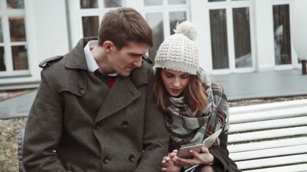 Romantico Coppia giovane seduta su una panchina bianca, con cappotto e cappello, freddo, stili di vita — Video Stock