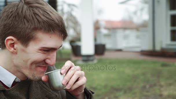 O homem está bebendo chá da garrafa térmica, sorrindo, olhando para a mulher. Tempo frio, close-up, estilo de vida, felicidade — Vídeo de Stock