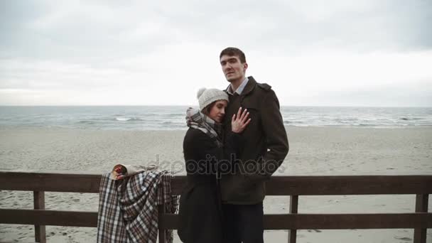 Pareja joven mirando al mar, caminando por la playa, abrigo y sombrero, clima frío del Báltico o Islandia — Vídeos de Stock