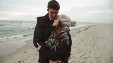 Genç çift Posing kadın fotoğrafçı için yürüyüş beach, palto ve şapka, Baltık veya İzlanda soğuk hava denize bakarak Günbatımı Fotoğraf oturumu