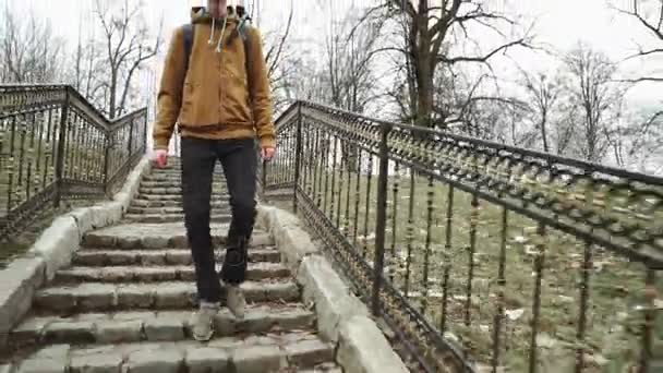 Sırt üstünde ilkbahar veya sonbaharda ağaçlar Sarı yapraklar, parkın içinden geri yürümek genç bir adamla merdivenlerden iner — Stok video