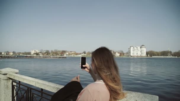 Ung vacker kvinna tar bilder med sin smartphone i stadsparken nära sjön — Stockvideo