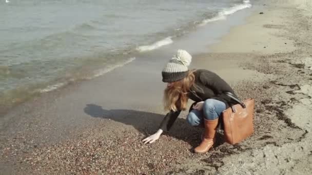 Uma mulherSentado e olhando seixos na praia Gaivotas voando e nadando no mar . — Vídeo de Stock