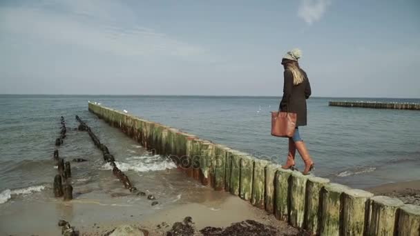 Una donna In piedi e camminando su frangiflutti di legno vicino al mare al tramonto. Gabbiani che volano e nuotano sul mare . — Video Stock