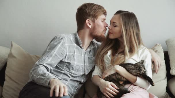 Casal está sentado no sofá em casa acariciando um gato, Kissingt e assistindo TV . — Vídeo de Stock