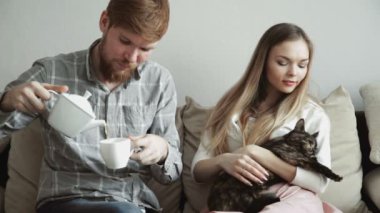 Çift evde kanepe kanepede oturan okşayarak bir kedi, dan bir beyaz çay çay içmek ve tv izlerken.