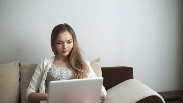 Ung kvinna sitter på soffan med laptop och ler — Stockvideo