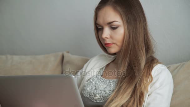 Jonge vrouw zittend op de Bank met behulp van laptop en glimlachen — Stockvideo