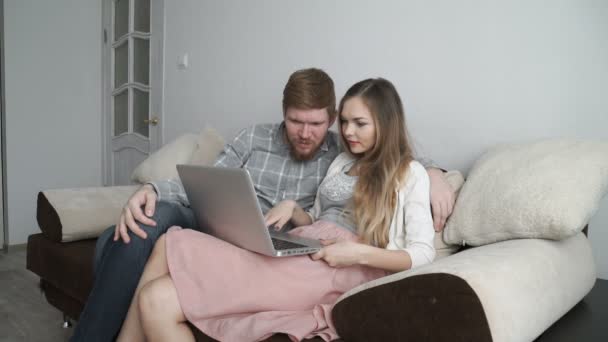 Paar sitzt zu Hause auf dem Sofa und schaut auf den Laptop-Bildschirm und lächelt — Stockvideo