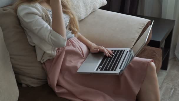 Молодая женщина сидит на диване с ноутбуком и улыбается — стоковое видео