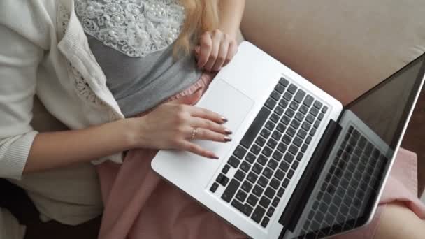 Młoda kobieta siedzi na kanapie za pomocą laptopa i uśmiechnięty, szczelnie-do góry ręce. Palce na klawiaturze — Wideo stockowe