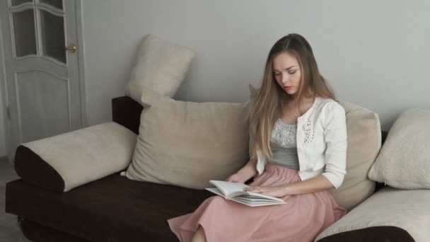 Hermosa joven sentada en el libro de lectura de sofá y sonriendo — Vídeo de stock