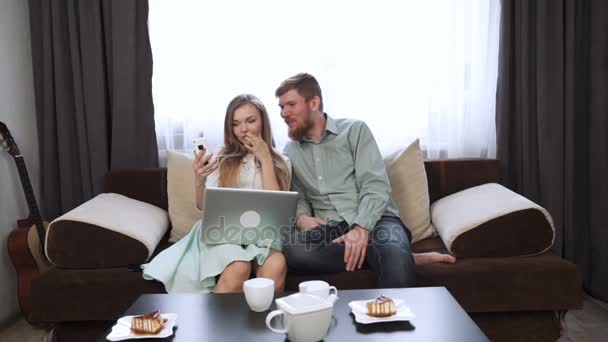 Casal está sentado no sofá em casa Olhe para a tela do laptop e sorria — Vídeo de Stock