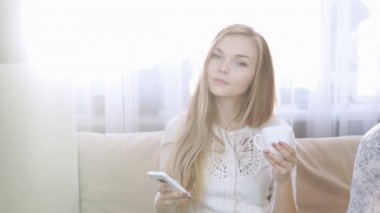 ev, teknoloji ve internet kavramı - gülümseyen kadın smartphone evde kanepenin üstünde oturuyor. Çay beyaz çay kümesinden iç. Güneş, güneş parlak ışıklar karşı ters ters