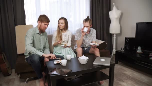 Amigos Dos tíos, hermanos, y una mujer joven están sentados en casa y tomando té, comiendo tarta de queso. Amigos de los estudiantes . — Vídeo de stock