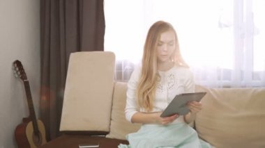 ev, teknoloji ve internet kavramı - gülümseyen kadın evde tablet ile kanepede oturuyor. Çay beyaz çay kümesinden iç. Güneş, güneş parlak ışıklar karşı ters ters