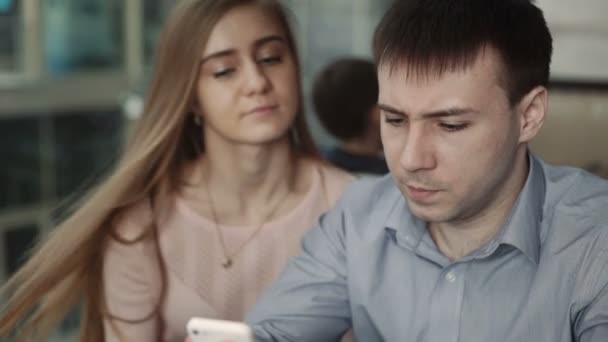 Atractiva pareja joven utilizando el teléfono inteligente en la cafetería Mira la pantalla sonriendo — Vídeos de Stock