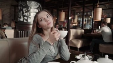Genç kadının birini bir kafede bekledi. Çay içiyor ve arkadaşlarınızla konuşurken. Gülümseyen ve kameraya bakıyor