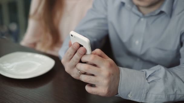 Manos de cerca, pareja joven utilizando el teléfono inteligente en la cafetería Mira la pantalla sonriendo — Vídeo de stock