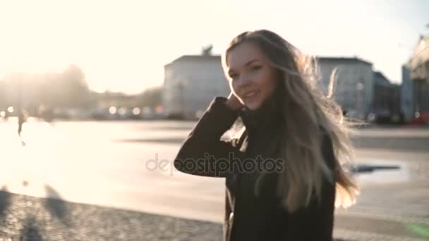 Gülümseyen ve kamera moda model şehir merkezinde gün batımında, poz genç güzel kadın uzun saçlı, gri paltolu ışık sıcak ve objektif parlama — Stok video