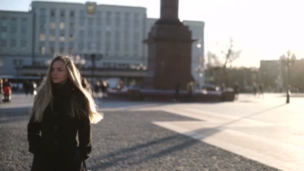 Молода красива жінка в сірому пальто з довгим волоссям, посміхаючись і позує на модель моди камери в центрі міста на заході сонця, тепле світло і відблиски на лінзі — стокове відео