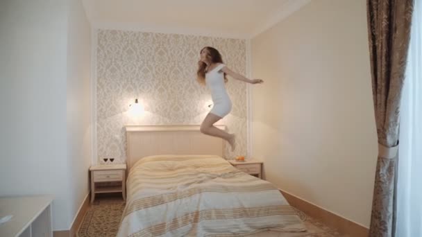 Молода жінка стрибає на ліжку в розкішному інтер'єрі кімнати . — стокове відео