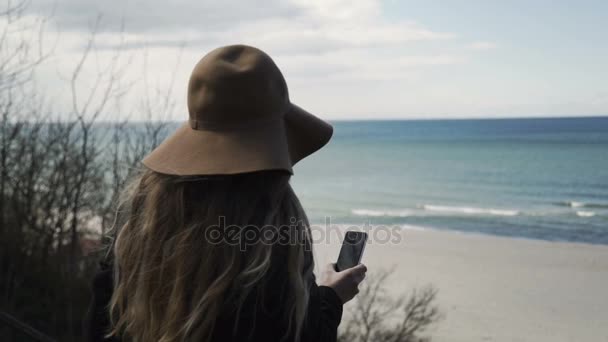 Самотня жінка з смартфон в руку дивиться на море зимових — стокове відео