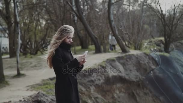 Una giovane donna guarda il mare da una roccia, in attesa di qualcosa. In un cappotto e con i capelli lunghi, un cielo blu . — Video Stock