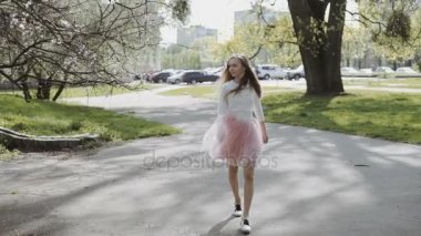 Genç ve güzel kadın pembe bir etek ve güneşli bir günde parkta bir smartphone giyen bir beyaz gömlek giyiyor. Üç eksenli Gimbal izleme atış stabilize