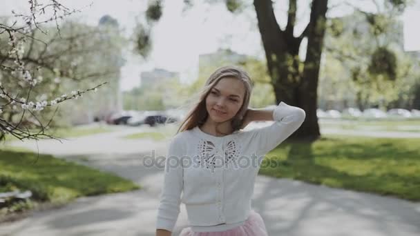 Jolie jeune femme en jupe rose et portant une chemise blanche portant un smartphone dans le parc par une journée ensoleillée. Plan de pistage stabilisé à trois axes Gimbal — Video