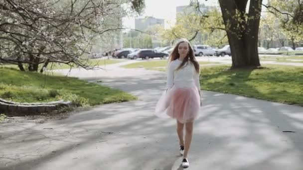 Mujer joven y bonita con una falda rosa y una camisa blanca con un smartphone en el parque en un día soleado. Tiro de seguimiento estabilizado Gimbal de tres ejes — Vídeo de stock