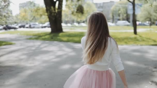 Pretty young woman in a pink skirt and wearing a white shirt wearing a smartphone in the park on a sunny day. Three-axis Gimbal stabilized tracking shot — Stock Video