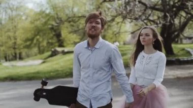 Genç çift elele yaz Park'ta yürüyordunuz aşık. Pembe tutu etek adam kadınla longboard eller üç eksenli stabilize Gimbal izleme atış