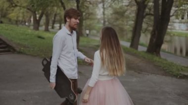 Genç çift elele yaz Park'ta yürüyordunuz aşık. Pembe tutu etek adam kadınla longboard eller üç eksenli stabilize Gimbal izleme atış