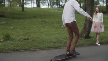 Genç çift elele yaz Park'ta yürüyordunuz aşık. Pembe tutu etek adam kadınla longboard eller üç eksenli stabilize Gimbal izleme atış