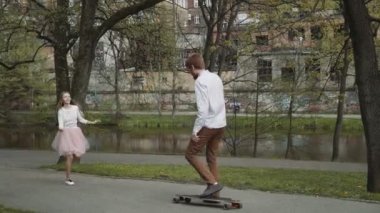 Genç çift elele yaz Park'ta yürüyordunuz aşık. Pembe tutu etek adam kadınla longboard eller üç eksenli stabilize Gimbal izleme atış