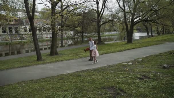 Jovem casal apaixonado andando no parque de verão de mãos dadas. Mulher de saia tutu rosa homem com longboard em mãos Três eixos Gimbal estabilizado tiro de rastreamento — Vídeo de Stock