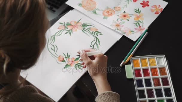 Eine junge Künstlerin malt mit Aquarell einen Wasserpinsel, Blumen, einen Kranz aus grünen Blättern. Nahaufnahme — Stockvideo