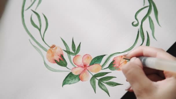 Uma jovem artista, pinta com aquarela pinta flores de um pincel de água, uma grinalda de folhas verdes. de perto — Vídeo de Stock