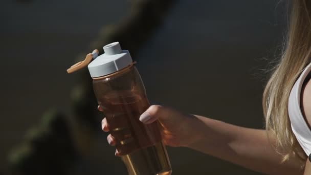 Sexy mladá žena v letní čepice a bílé bikiny plavky, koupu slunce, pije vodu z láhve. — Stock video