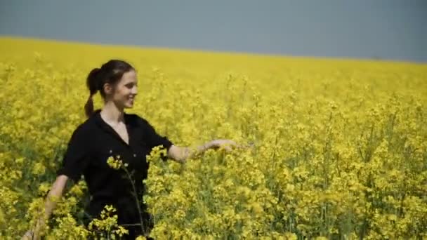 Jeune femme en salopette noire qui court à travers le champ jaune touchant des fleurs HD 