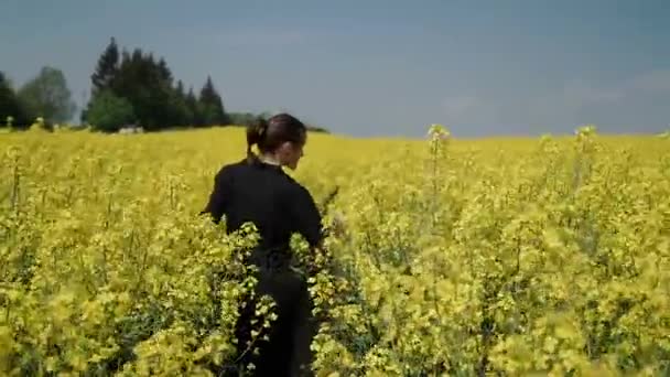 Jeune femme en salopette noire qui court à travers le champ jaune touchant des fleurs HD 