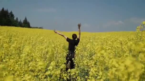 Jeune femme en salopette noire qui court à travers le champ jaune touchant des fleurs HD 